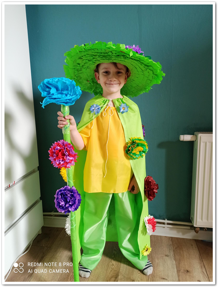 Chłopiec w przebraniu Pana Wiosny. Peleryna i kapelusz w kolorze zielonym, ozdobione kolorowymi kwiatami.