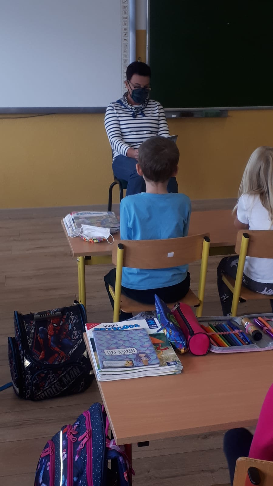 Pani bibliotekarka czyta dzieciom siedzącym w ławkach książkę