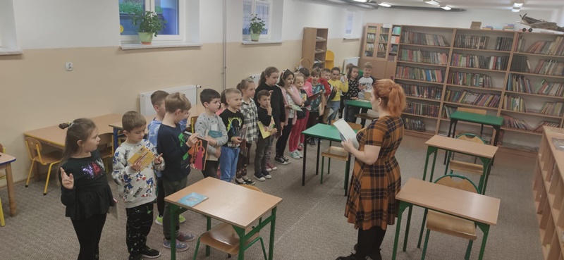 Pierwszoklasiści stoją w rzędzie, w dłoniach trzymają książki