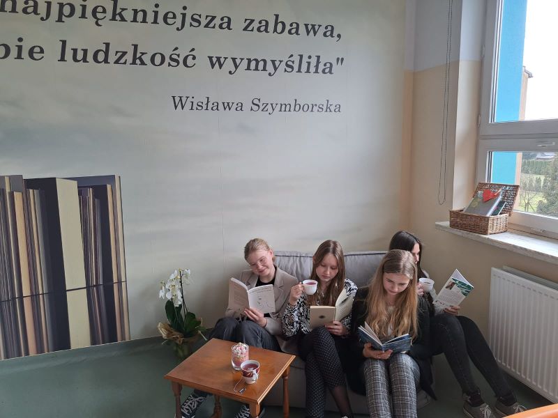 Cztery uczennice siedzące przy stoliku, w rękach trzymają otwarte książki i filiżanki z herbatą
